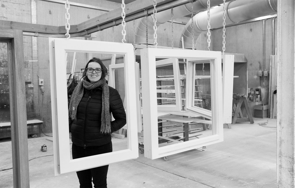 Black and white photo of smiling women standing in hanging window frame in workshop