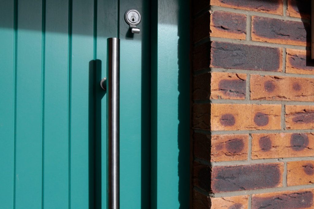 Silver long door handle - silver keyhole cylinder - turquoise door and frame - brick wall