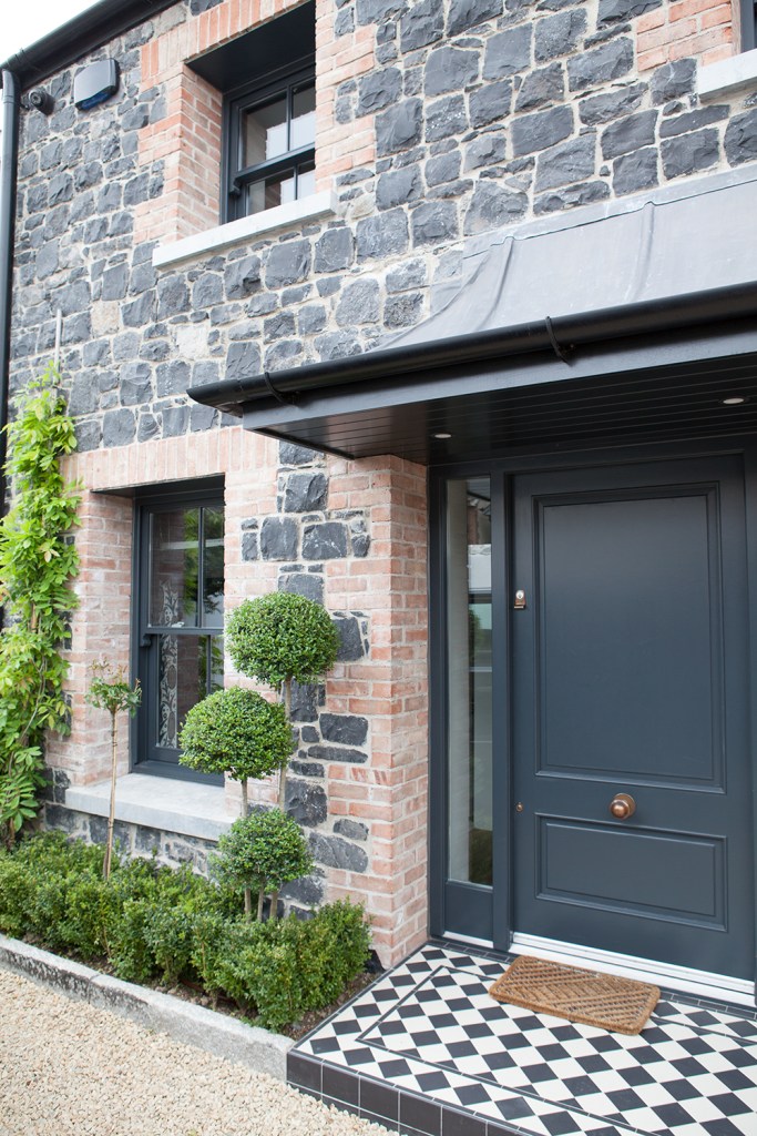 Vintage style front door and screen - black and white checkered tile floor - sidelite windows - black stone and brick wall