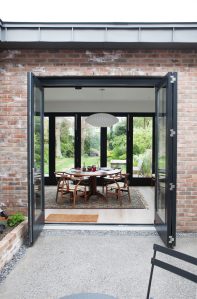 Open glass bi-fold door with black frame and red brick wall