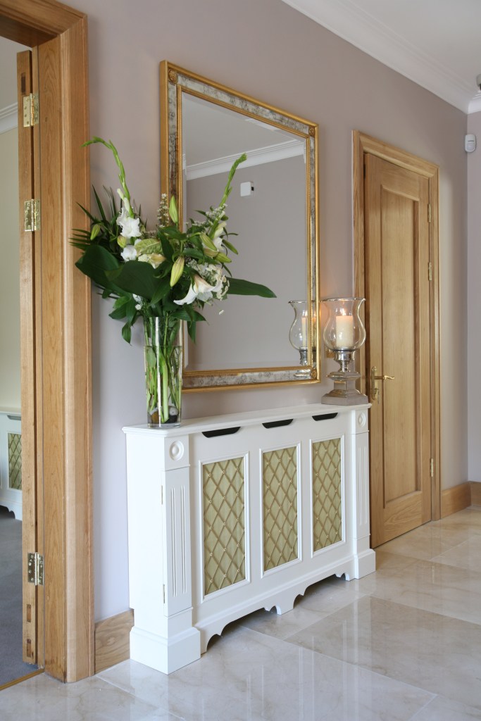 White radiator cover with mirror above and flowers with vase and candle
