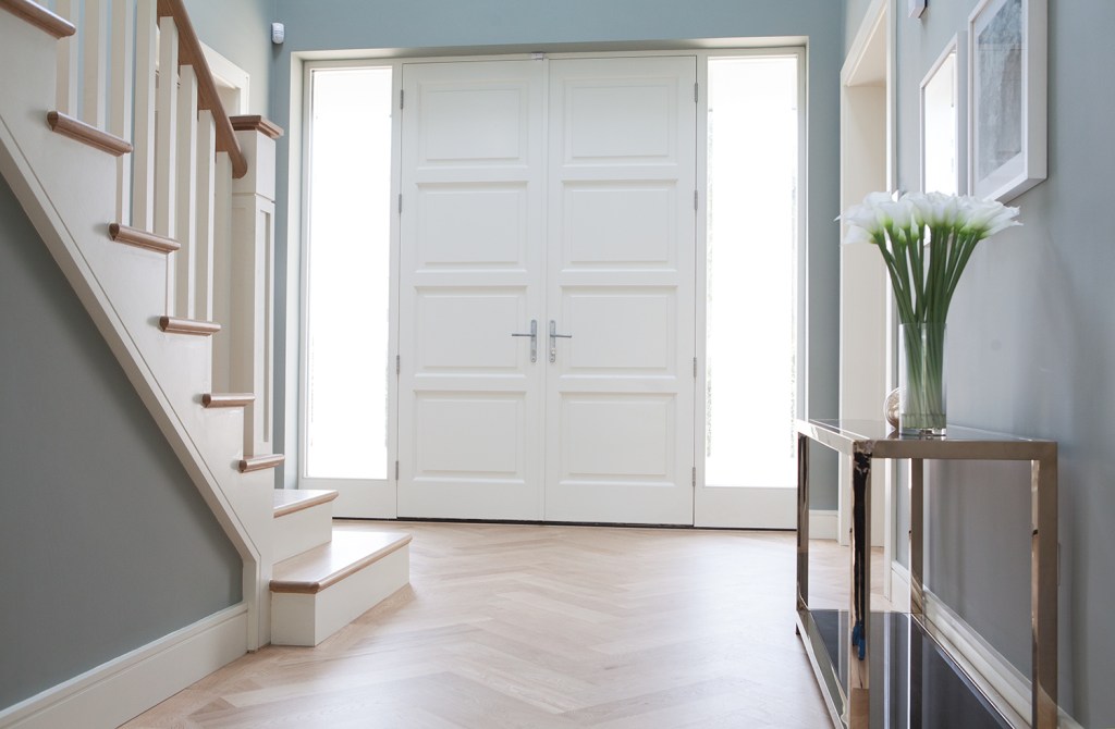 white double door with sidelite windows and staircase with hallway table with white flowers