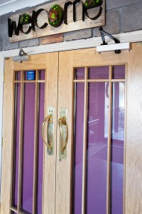 front door view - double pull doors with golden door handle - wooden door frame and grille - silver door arm hinges - welcome board above door