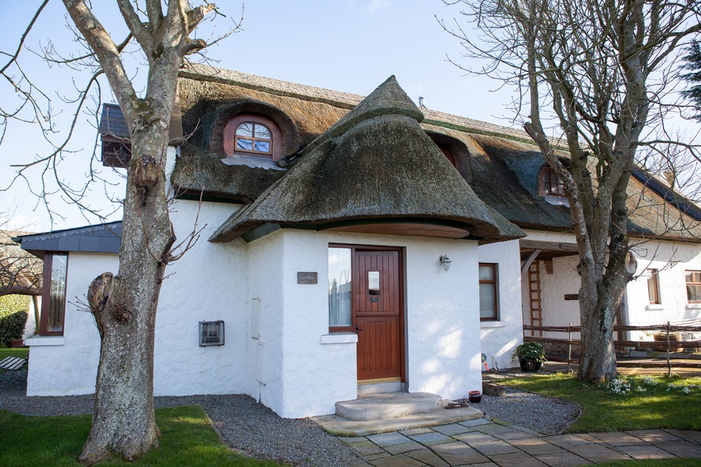 Thatched roof house with white walls - steps to front door - gravel - two tree's in the front yard - sidelite windows