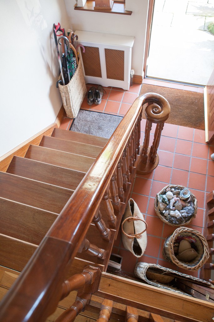 Staircase view from the top - wooden staircase handrail - wooden baluster - wooden tread - tiled floor - front door - umbrella's in a basket