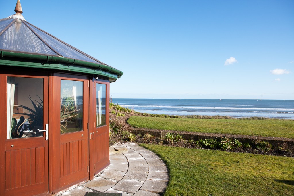 Curved wooden cottage - paving outside - grass landscape - view of the ocean - Transom doors