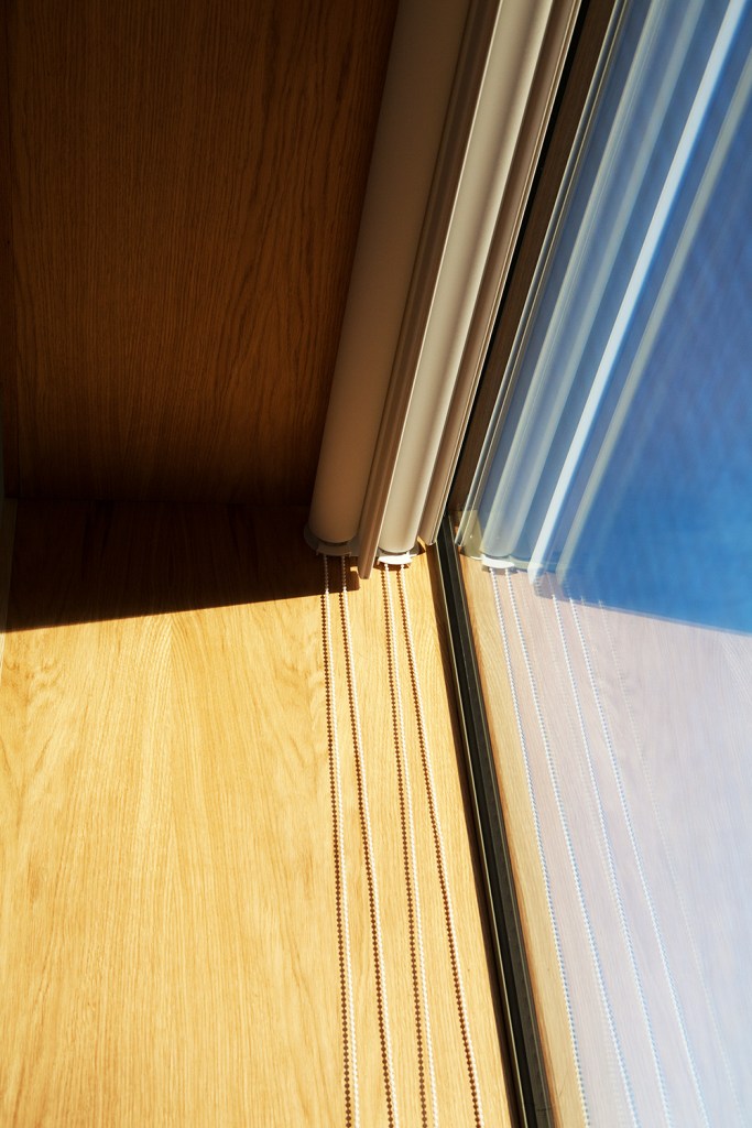 corner of window with wooden casing and opened window blind with strings hanging down