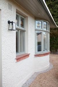 White textured wall with red brick window sill and green window frames - lantern shape light hanging from side wall