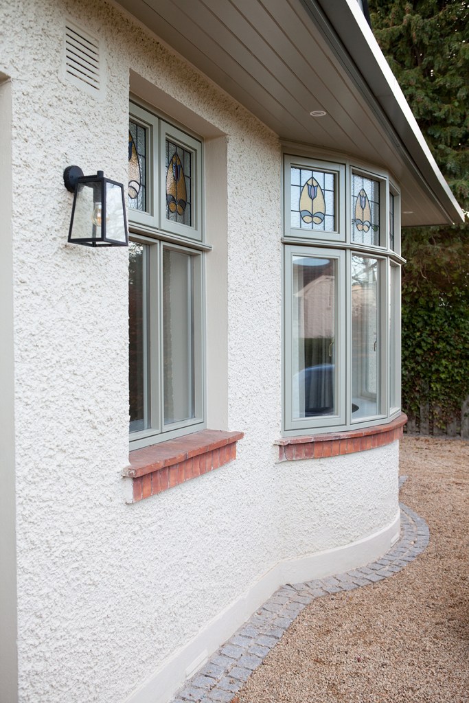White textured wall with red brick window sill and green window frames - lantern shape light hanging from side wall