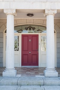 Two big white pillars in front of house with red door and sandblasted sidelite and transom window