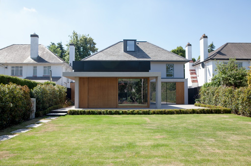 Green grass landscape - small bush hedges and walkway - glass wall windows - sheeted wood walls - sliding glass door