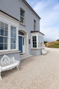 Side view of house - garden double chairs sitting in front of house - windows with white frame and grills - blue door with fanlight and sidelite windows