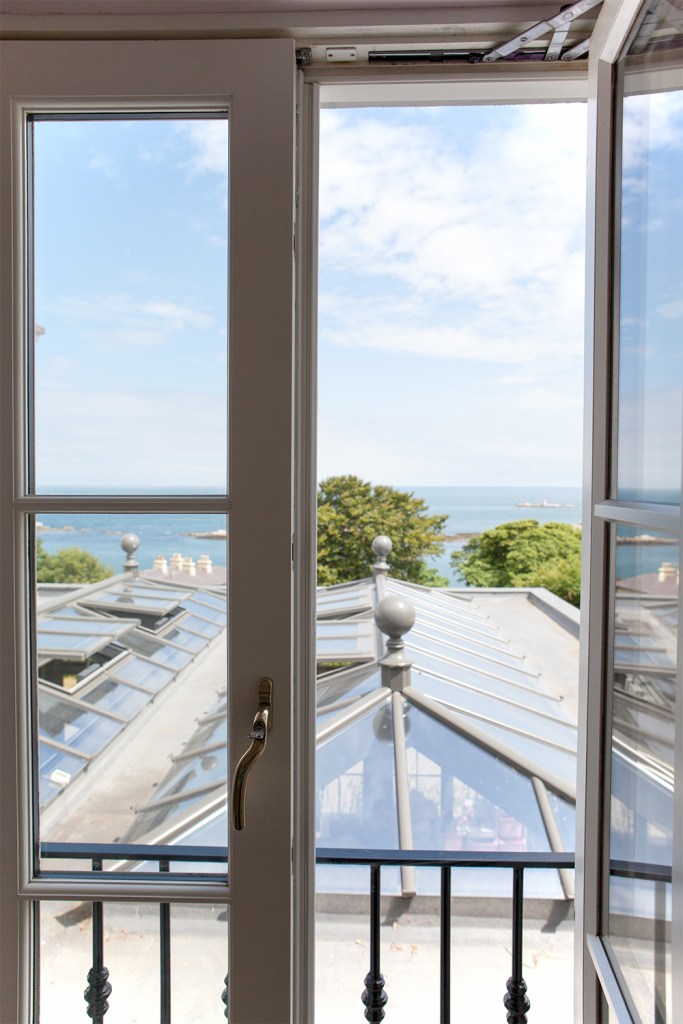 Glass window opened - looking over ceiling windows and the ocean - white window frame and grills - iron baluster