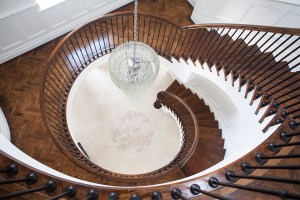 Looking down from spiral staircase - dark wood staircase landing - dark wood stair tread and handrail - iron baluster - hanging chandelier in the middle