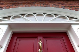 Red front door with brick wall casing - white transom window arch - gold door knob and handle - white door frame