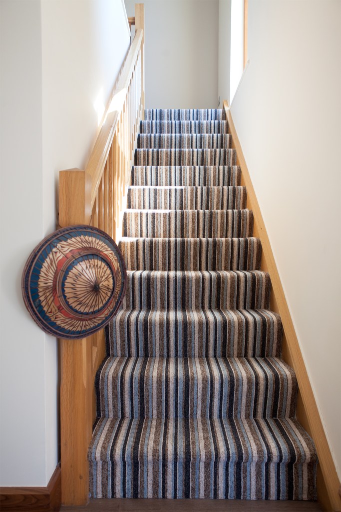Hanging hat on staircase balustrade - striped carpet on staircase - wood staircase handlebar and balustrade