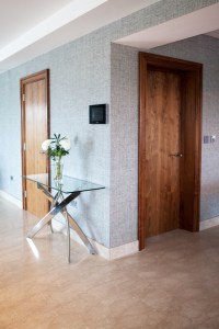 Two inside interior wooden door with wood frame - glass table top - silver table legs - white flowers in vase - laminated floor - grey wall