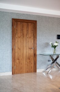 Interior wooden door with wooden door frame and glass table on the side - white flowers in vase - laminated floor - grey wall