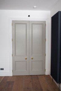Grey side by side door with wood panel and gold door knobs - white door frame - wood laminated floors - white wall