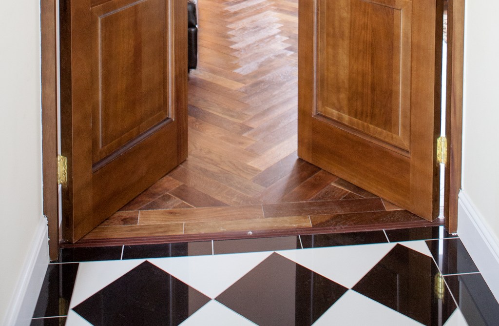 Black and white checkered floor tile - wood laminated floor - wood double swing door - white skirting - gold door hinges