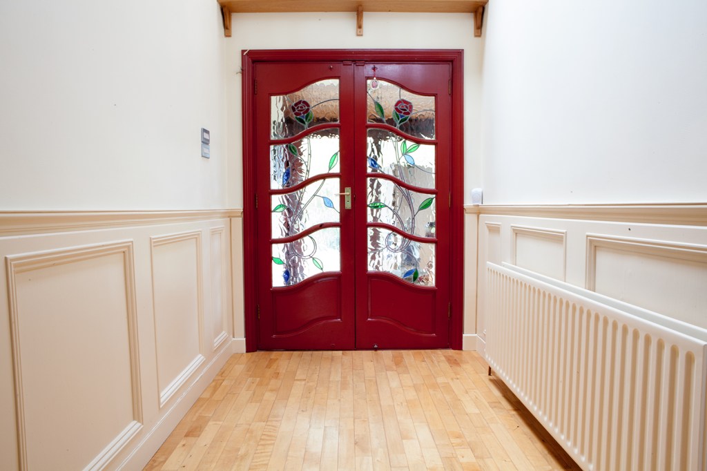 Red door with stained rose glass windows - side by side door - gold door handle - white radiator - half wall panel - red door frame - laminated wood floor