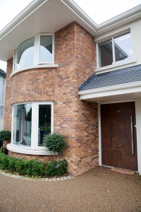 Curved windows with white frame and curved brick wall - wooden pivot door - double story house - gravel