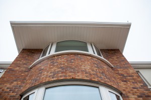 Looking up at curved window - white window frame - brick wall - curved brick wall - white extended roof