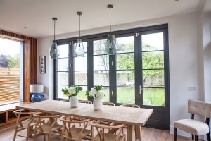 Wall window with wood frame detail - closed stacker doors with black frame and grille - dining room set with wooden chair - white and green flower table arrangements