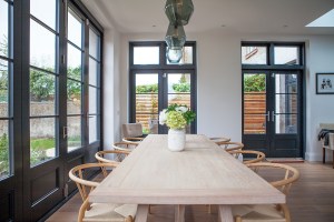 Long wooded dining table and chairs with white and green flower arrangement - transom doors with black frame and grilles - transom stacker door