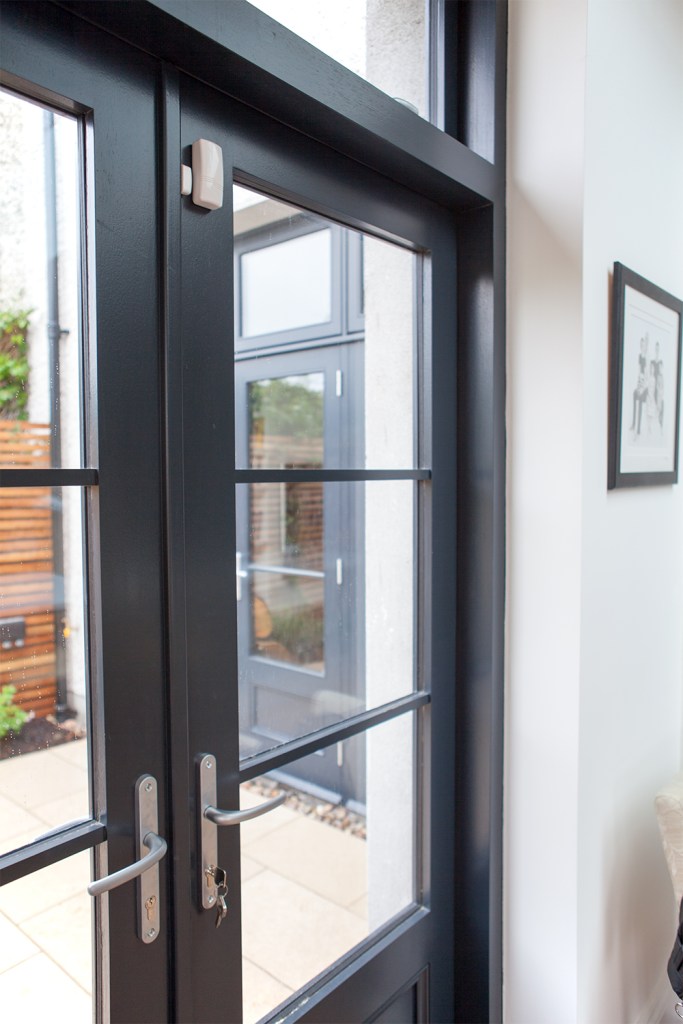 Black double door with black frame and grille - transom door - windows in door - silver door handle - white wall - side view