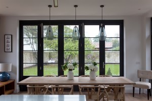 Natural light coming through closed stacker doors - wood dining room table and chairs - three hanging lights - view of garden - transom door