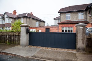 Driveway gate - automated sliding gate - black double length gate with pillars on side - red brick house - sidewalk view - driveway entry