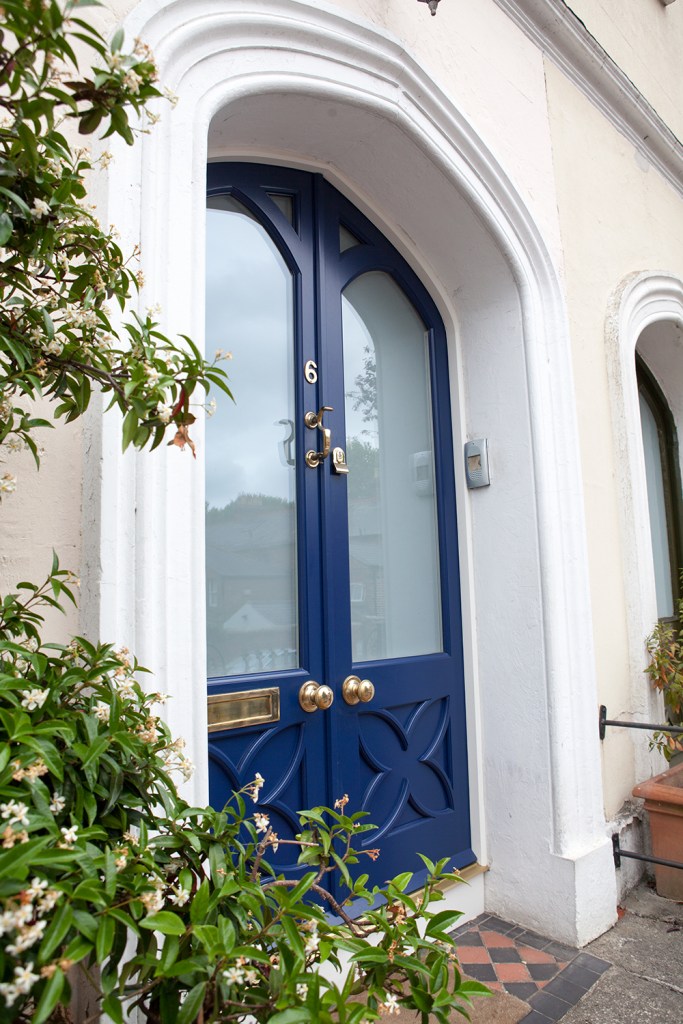Blue front door with stained windows and gold door handles and knockers - White arch above door - small bush