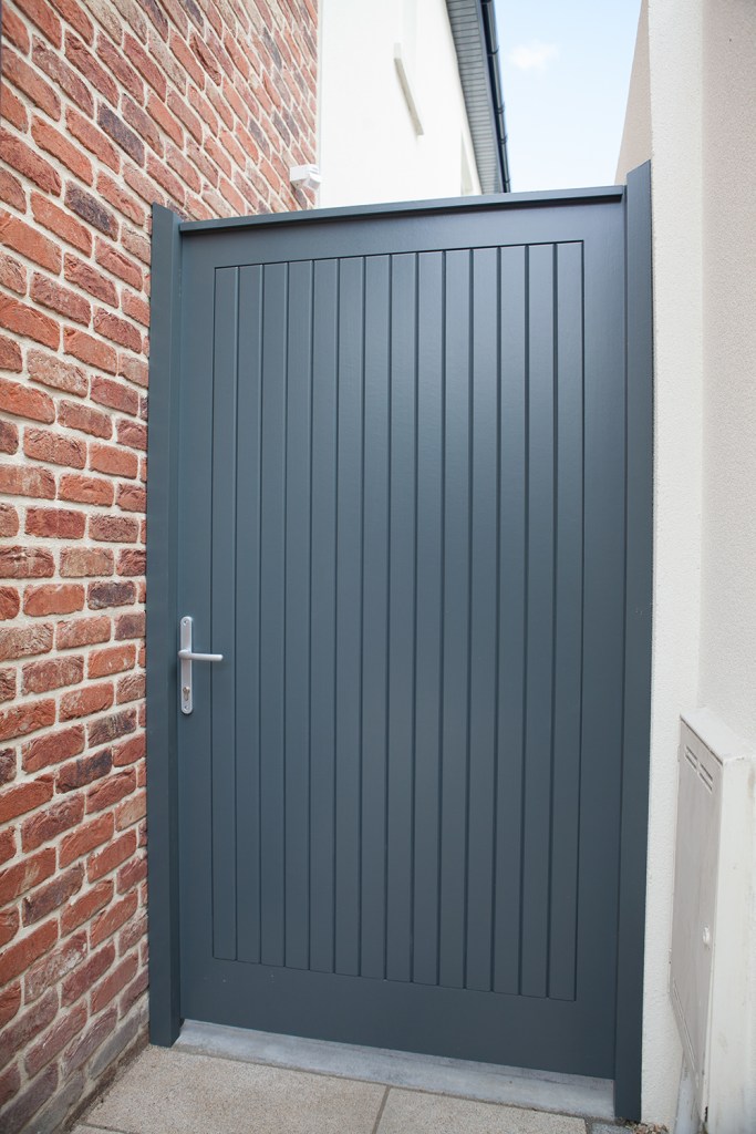 Black back gate with black frame and silver door handle - red brick wall - white wall - outside gate