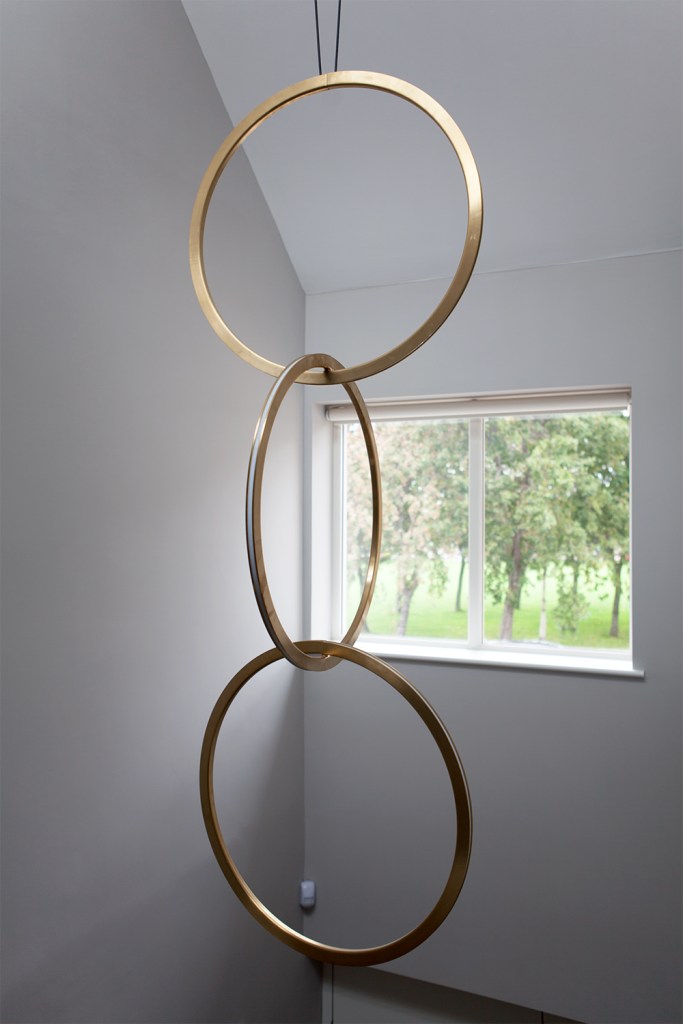hanging golden rings - golden ring art piece - ceiling window - white ceiling and wall - interlinked golden rings