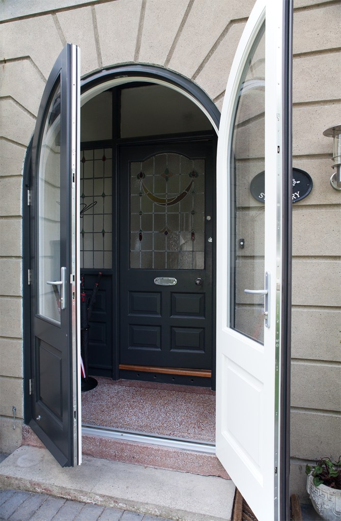 Double door swung open - black outside door - white inside of door - transom doors - entrance way - brick arch