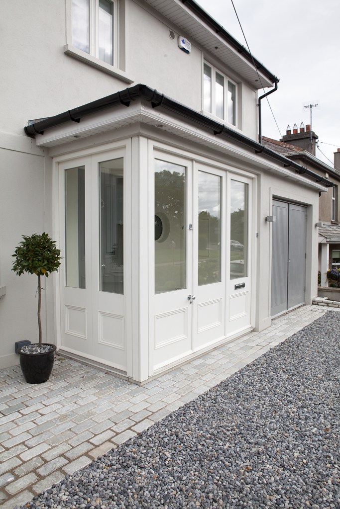 View from side - transom door - windows with white frame - gravel - tree in pot in corner - garage door - black roof gutters