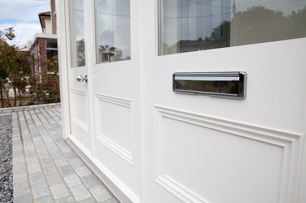 white door with silver mail receiver and silver door knob - transom door - windows in door - carving in door - brick sidewalk - side view