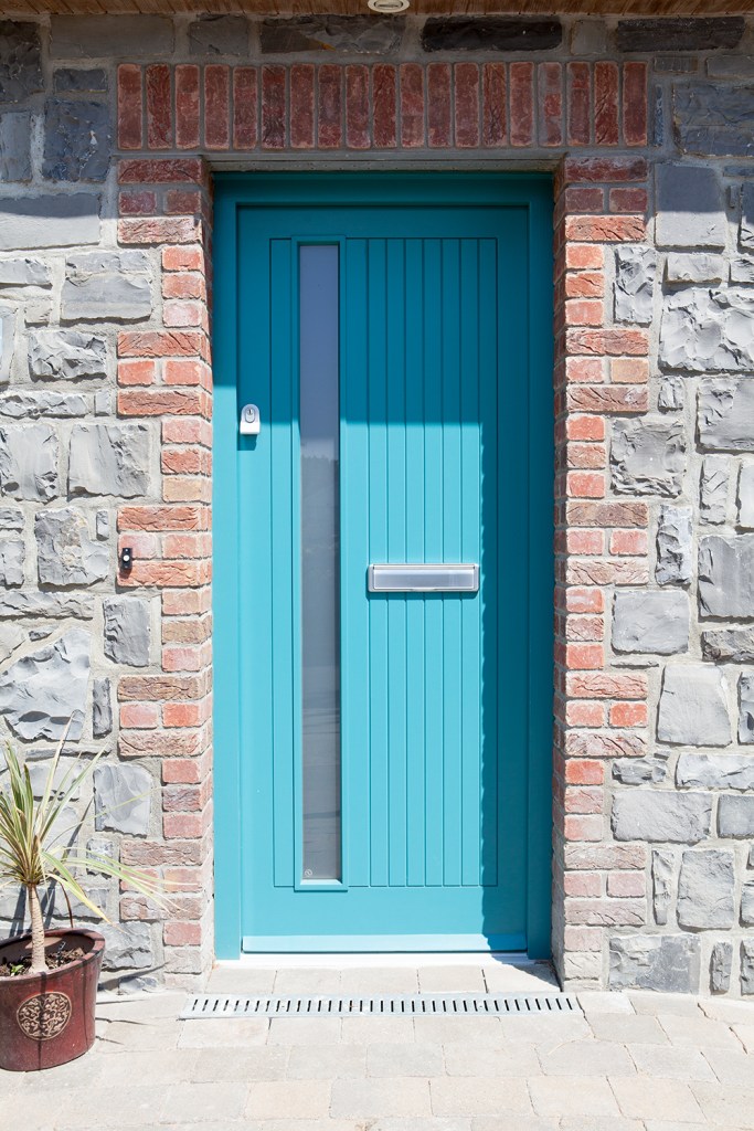 single turquoise door with thin tall window and silver mail receiver - red brick arch around door - stone house