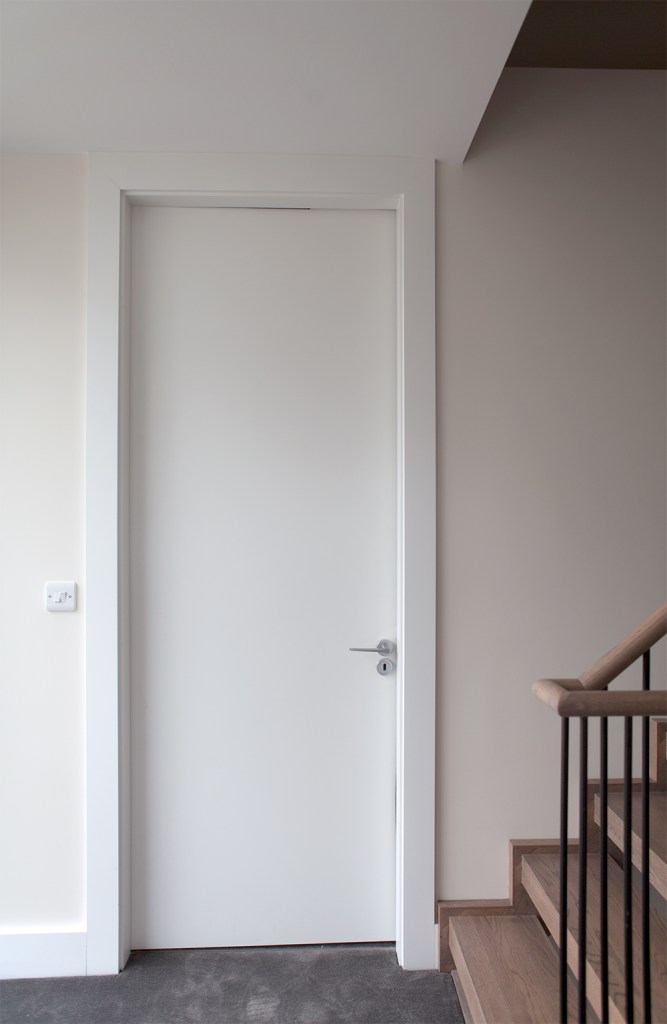 white door with a white frame - white skirting - wooden stairs - stair railing