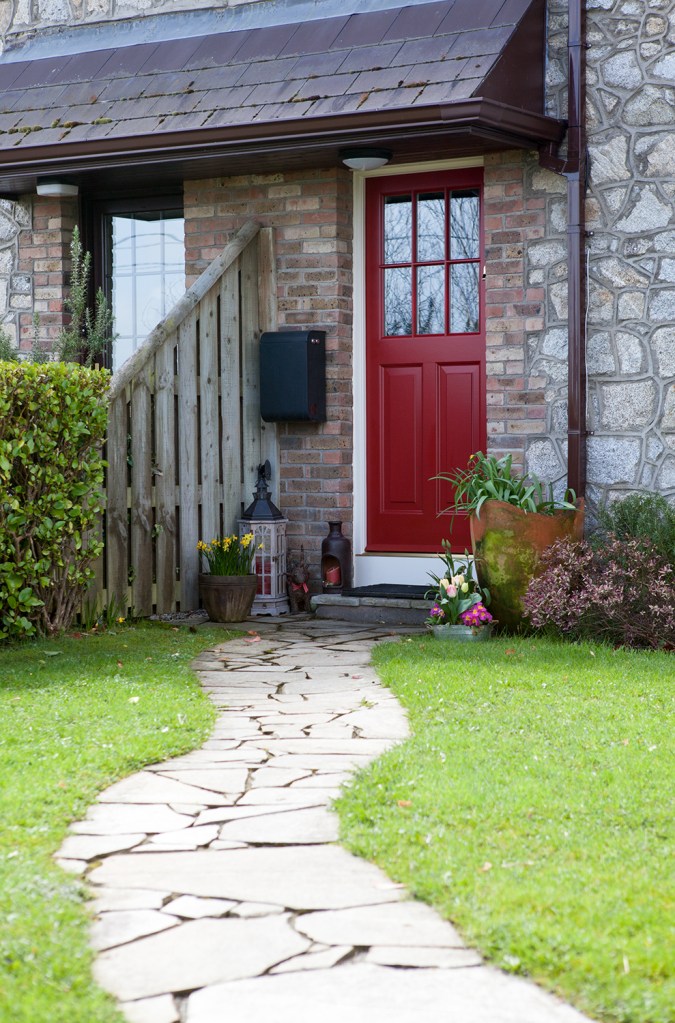 stone pathway leading to red door with white frame and windows at top half of the door - green grass and landscape - flowers at front door