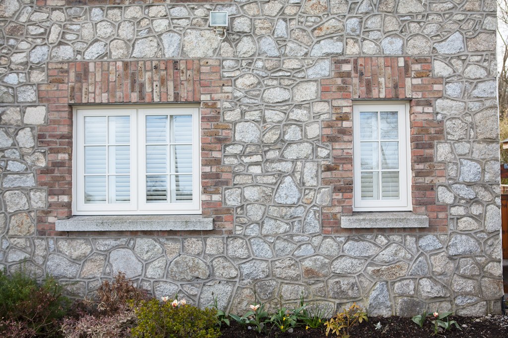 white frame window with cement apron and white grills - window surrounded with red brick - stone wall - garden bed