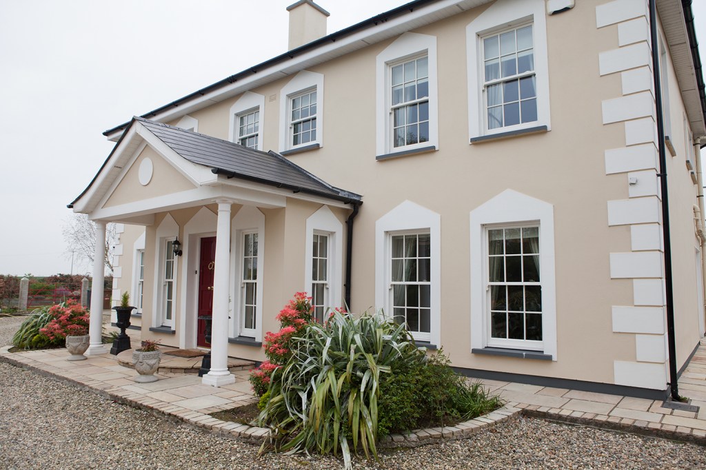 side view of double story house - black porch roof - pillars - pink flowers - double hung windows with white frame