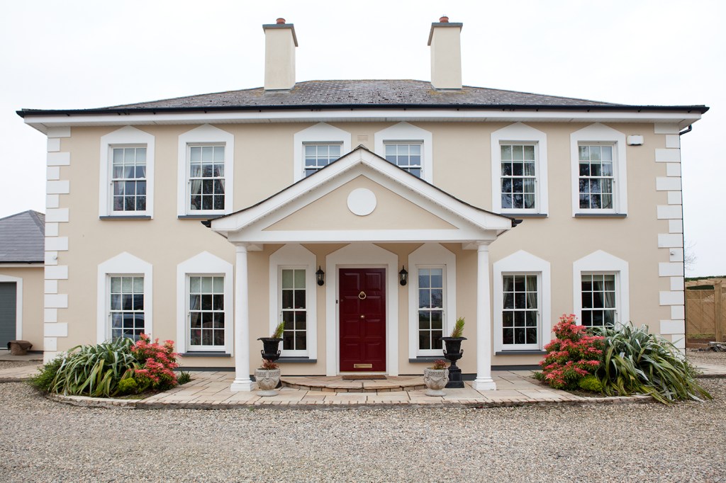 red door - big house with allot of windows - porch in front of door - two chimneys - gravel road