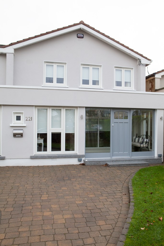 Front view of house - transom grey door with two big sidelight windows on the side - brick driveway - tall windows - white window frame