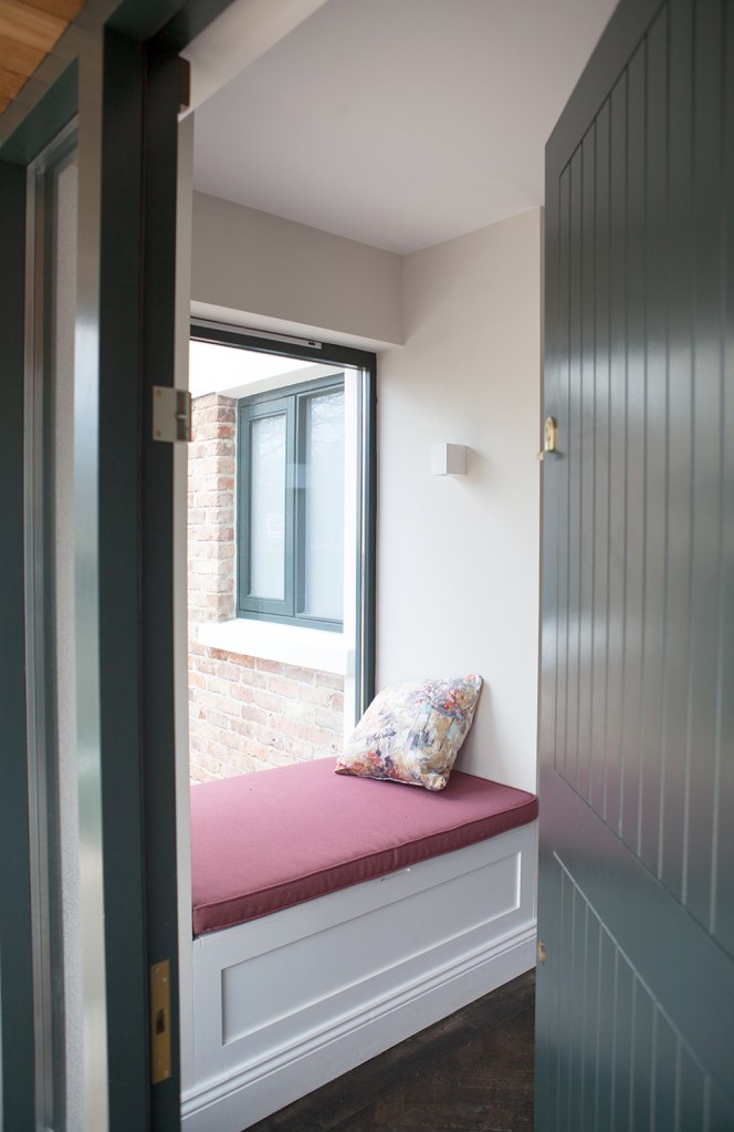 Black door with black frame opening up to a view of a reading nook on window bench - window bench attached to big window - white arch - white ceiling