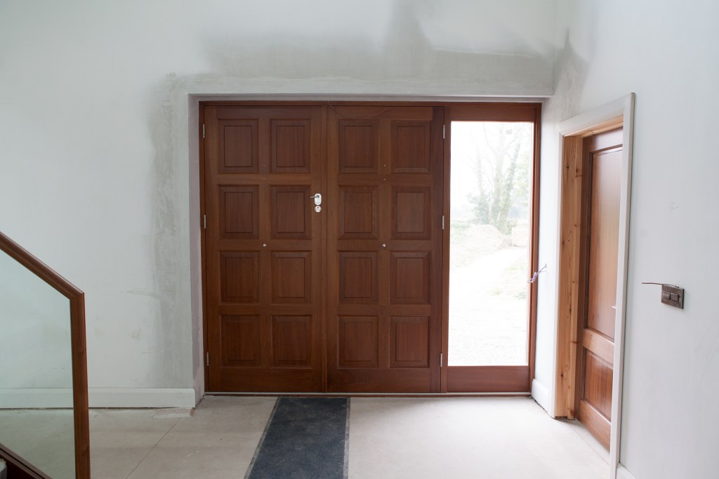 Double wood door with a window that is door length next to it. View is from inside.